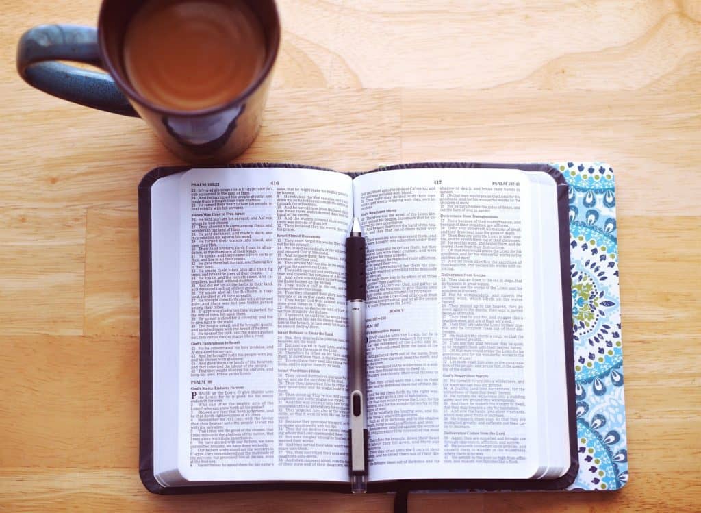 Image of an open Bible and a cup of coffee on a wooden table as seen from above.