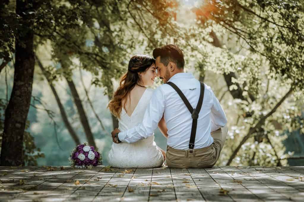 Image of newlyweds sitting on a dock with backs facing camera.