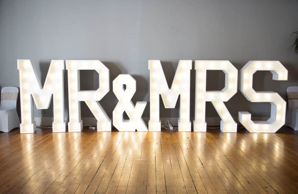 White lighted marquee sign that says "Mr. & Mrs." against gray background and wood floor.