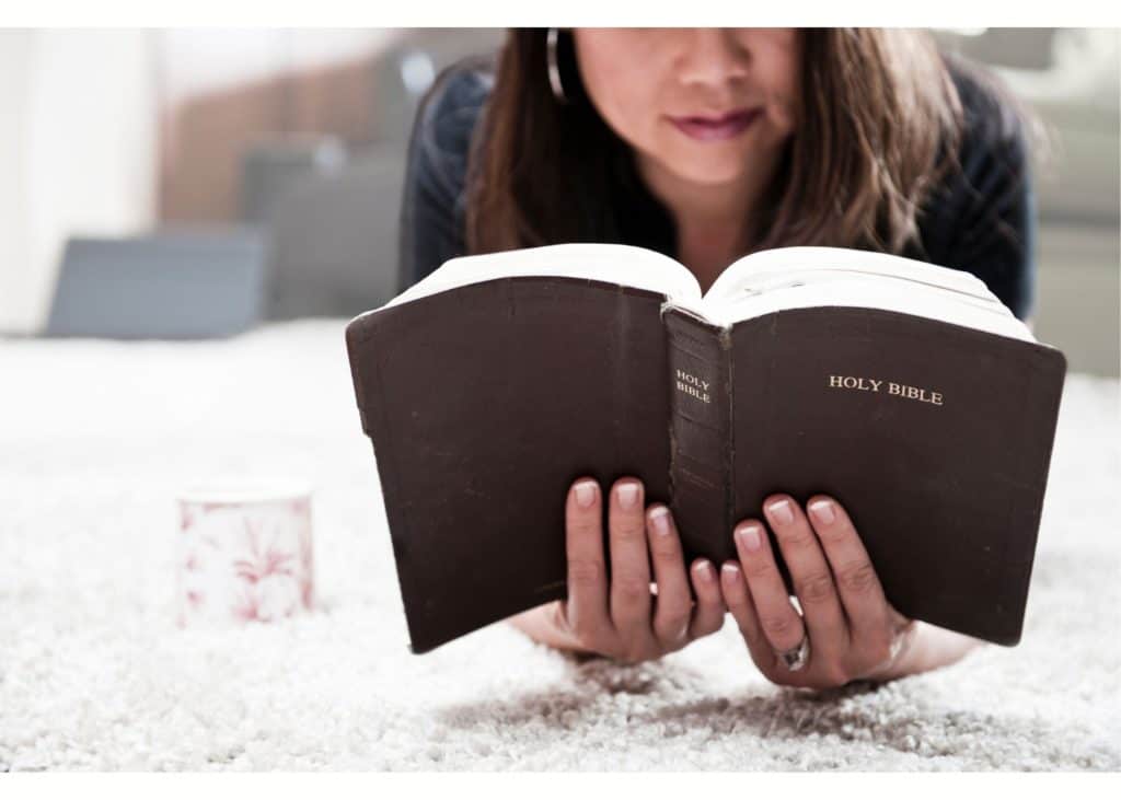 Image of a woman lying on the floor reading a Bible and drinking coffee.