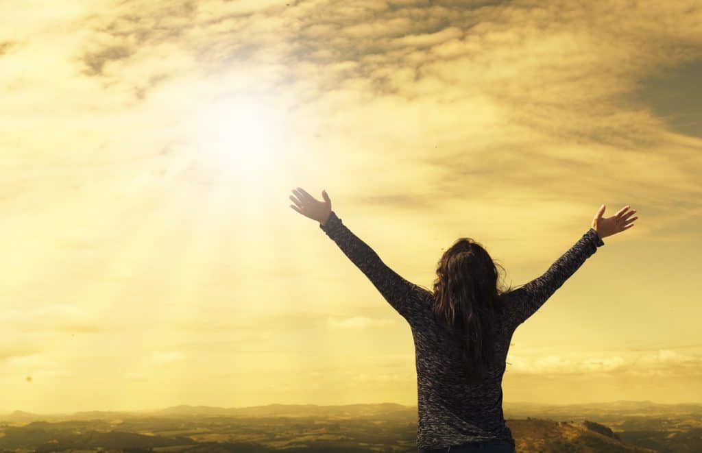 Woman with arms raised praising God outside at sunrise.