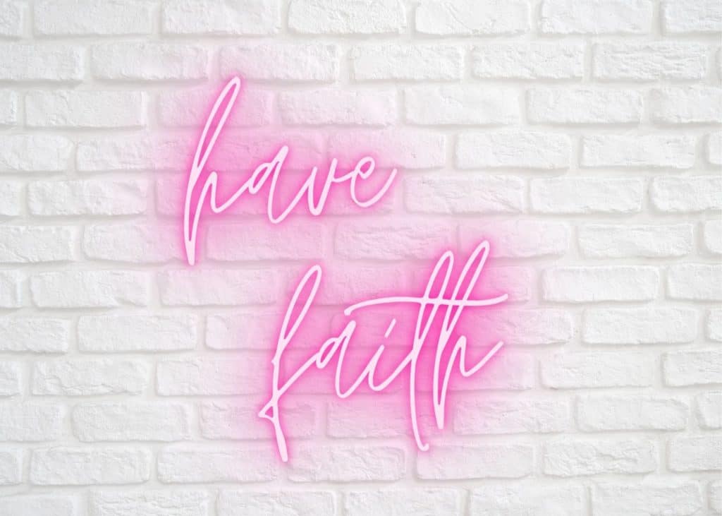 Neon pink sign that says "have faith" against a white brick wall.