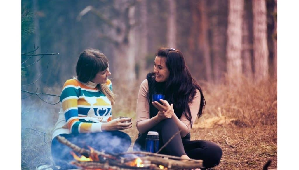 Two women sitting by a campfire talking.