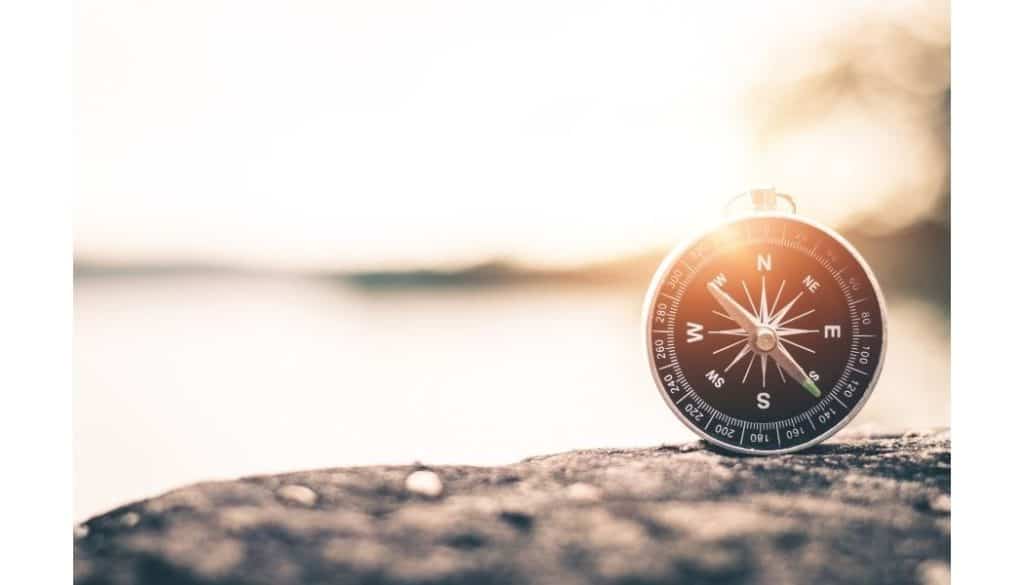 Image of a compass on a rock with a sunset in the background.
