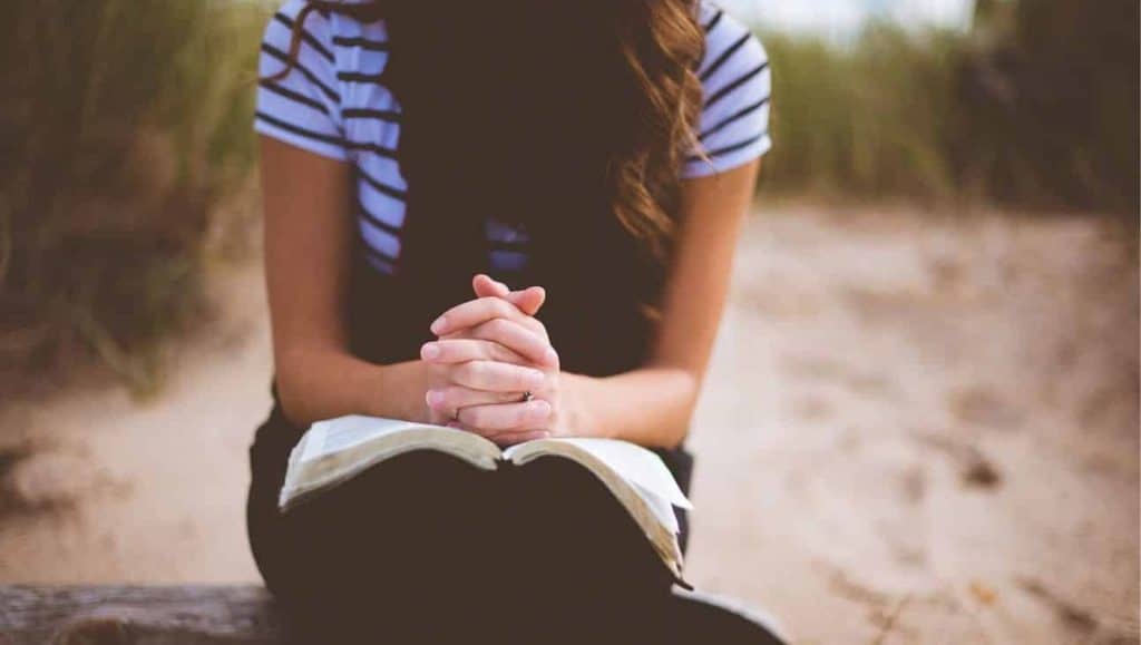 Woman praying with a Bible in her lap.
