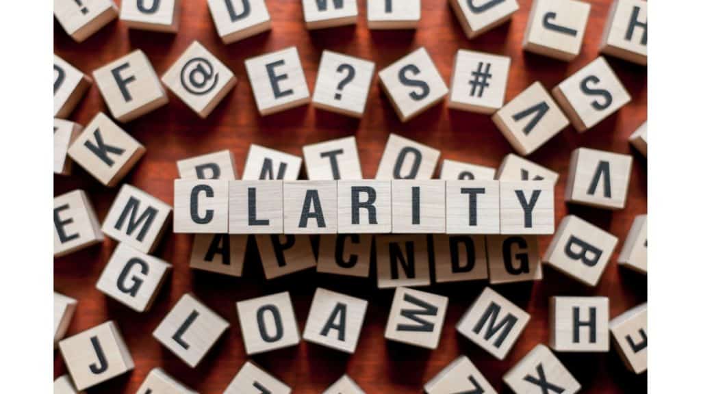 Image of letter tiles that spell out the word "clarity on top of random letter tiles spread out on a wooden table.