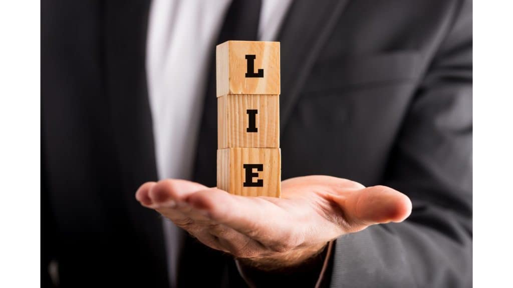 Close-up picture of a man in a suit holding blocks spelling out the word "lie" in his hand.