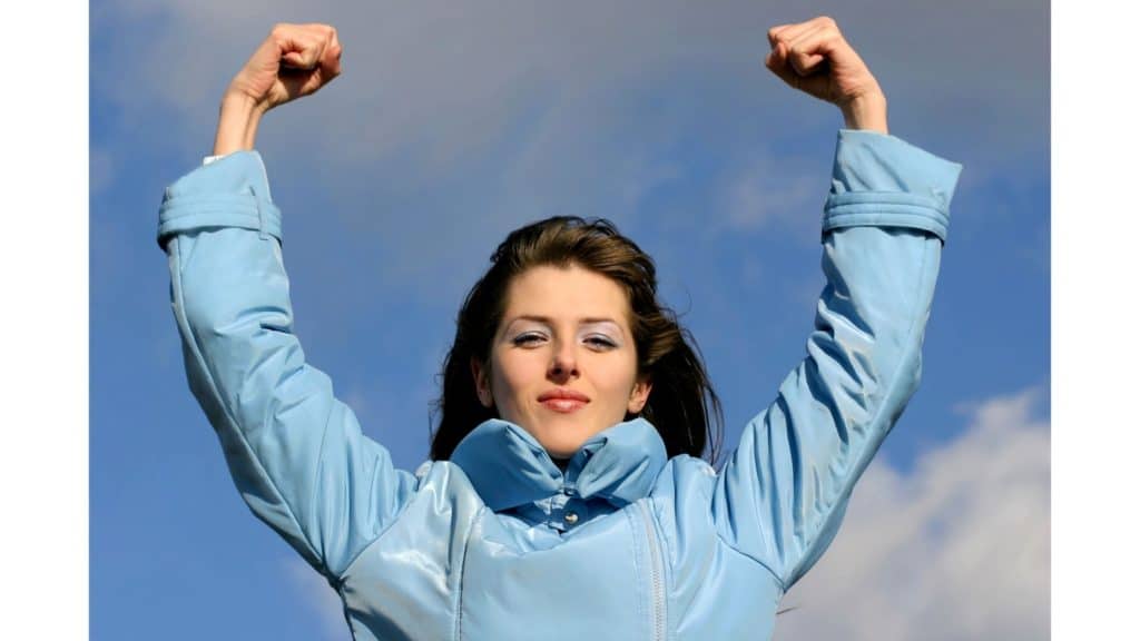 Woman standing with arms raised as if to show her strength.