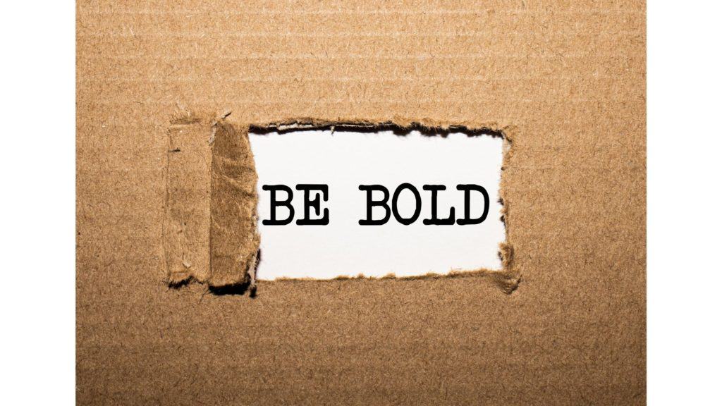 Cardboard with a hole cut in it and the words "be bold" showing through the hole.