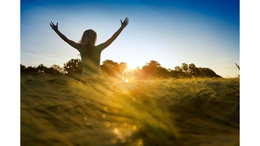 Woman standing in field at sunset with arms raised seeking a relationship with God.
