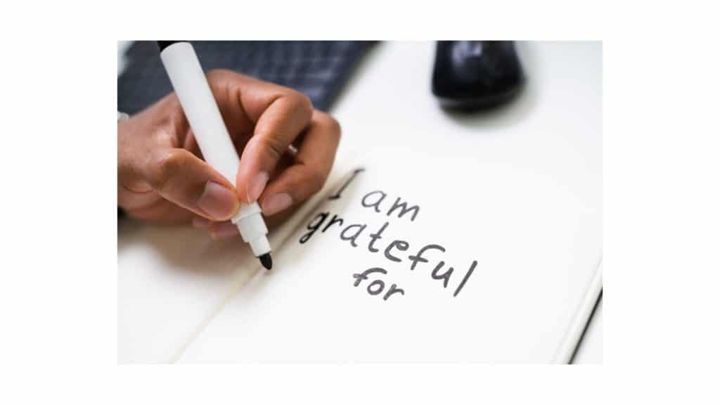 A woman writing "I am grateful for" in a gratitude journal.
