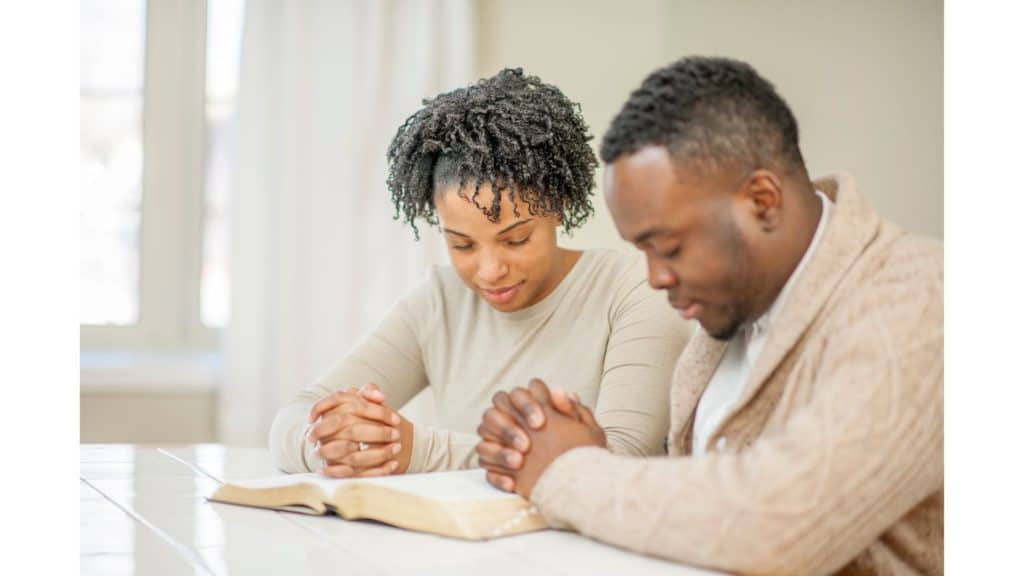 Married couple praying over an open Bible.