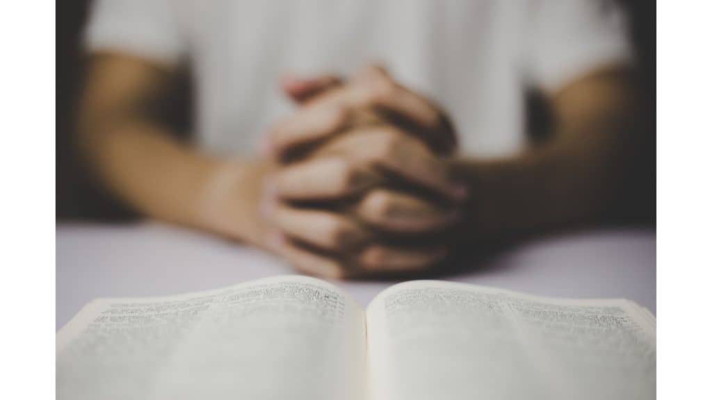 Hands praying in front of a Bible.