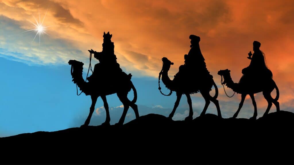 Silhouettes of the 3 wise men riding camels against a sunset sky.