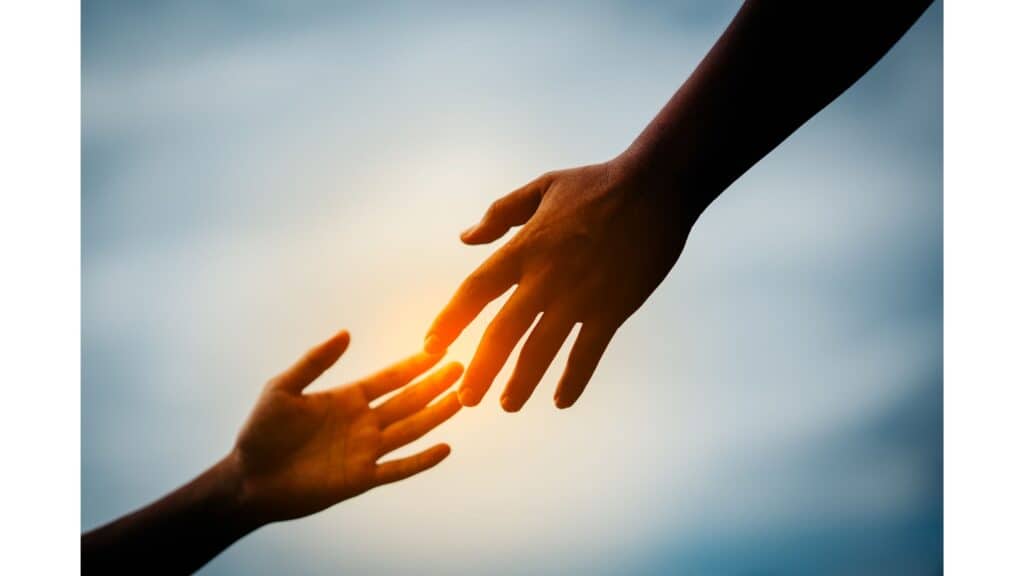 Hands reaching out to one another with sunset in background.