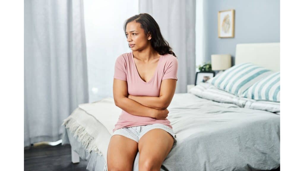 Woman sitting on the side of a bed with a worried look on her face.