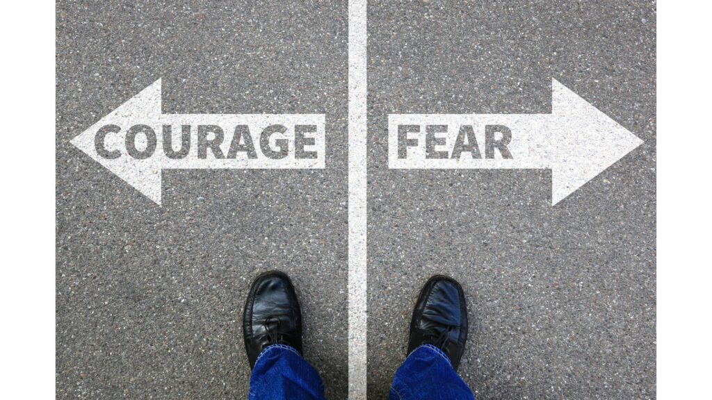 Photo from above of a line on the pavement with an arrow and the word "fear" pointing to the right and an arrow with the word "courage" pointing to the left.