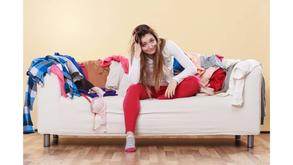 Woman smiling sitting on a sofa covered in laundry.
