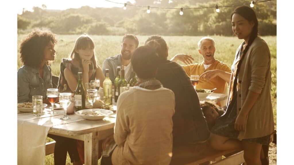 Couples sitting around a table outside in the late afternoon enjoying a meal and wine together.