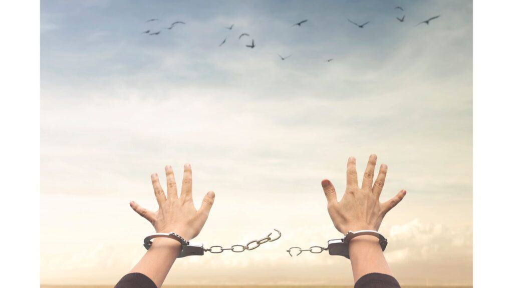 Hands in handcuffs reaching out towards the sky, but the chain between the handcuffs is broken.