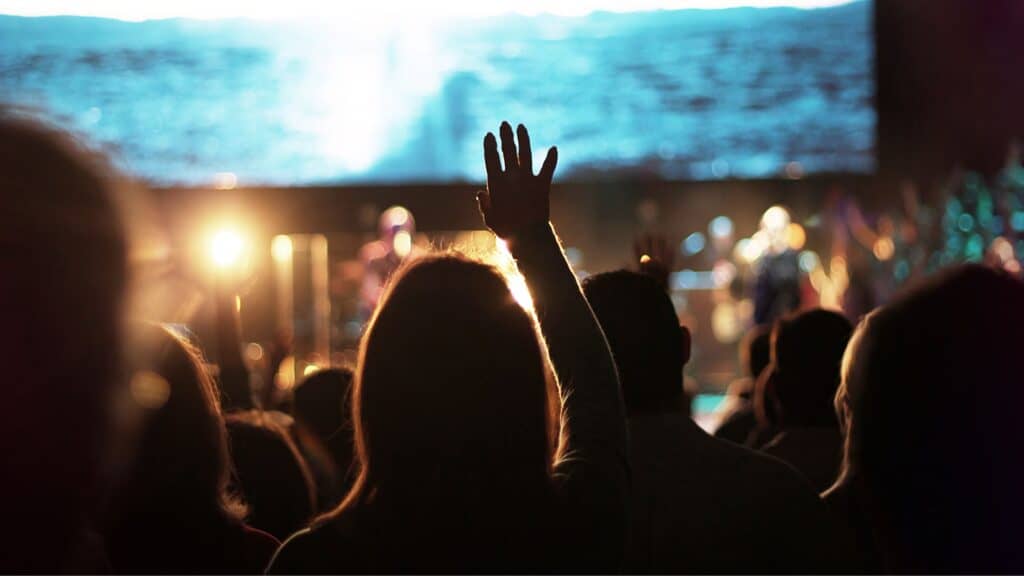 Image of a person with hands raised in worship, depicting current church culture (nondenominational).